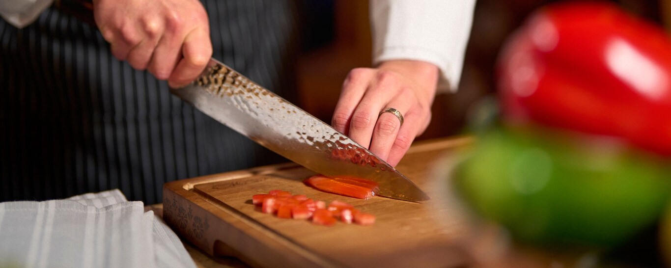 A chef slicing bell peppers on a wooden cutting board with a large knife